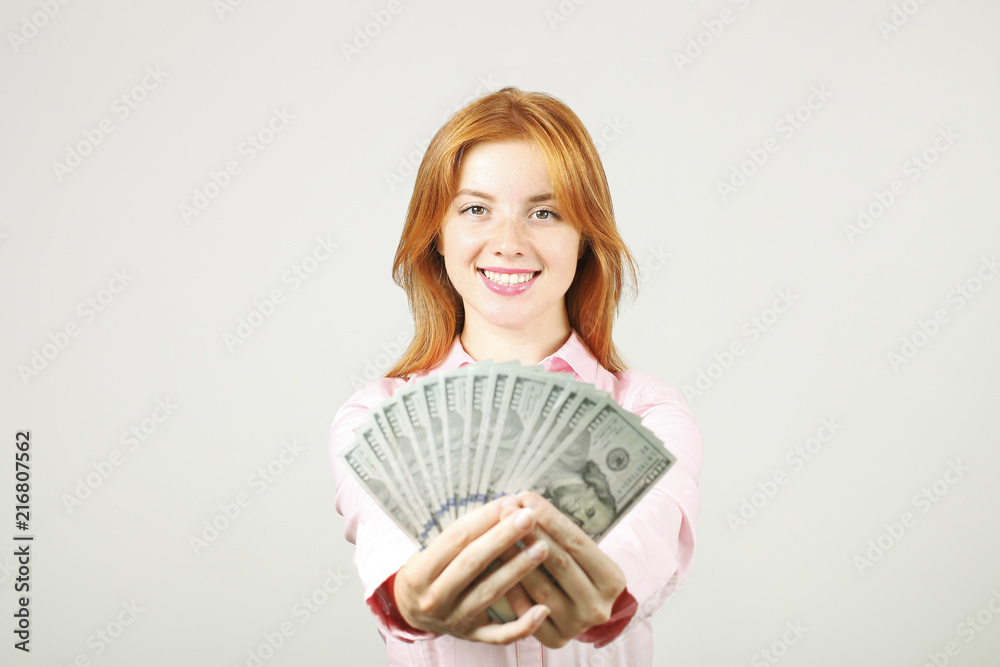 Portrait of young beautiful redhead woman with fistful of money holding one hundred dollar bill stack like fan. Excited attractive red hair female w/ lots of cash. Background, copy space, close up. Portrait of young beautiful redhead woman with fistful of money holding one hundred dollar bill stack like fan. Excited attractive red hair female w/ lots of cash. Background, copy space, close up.