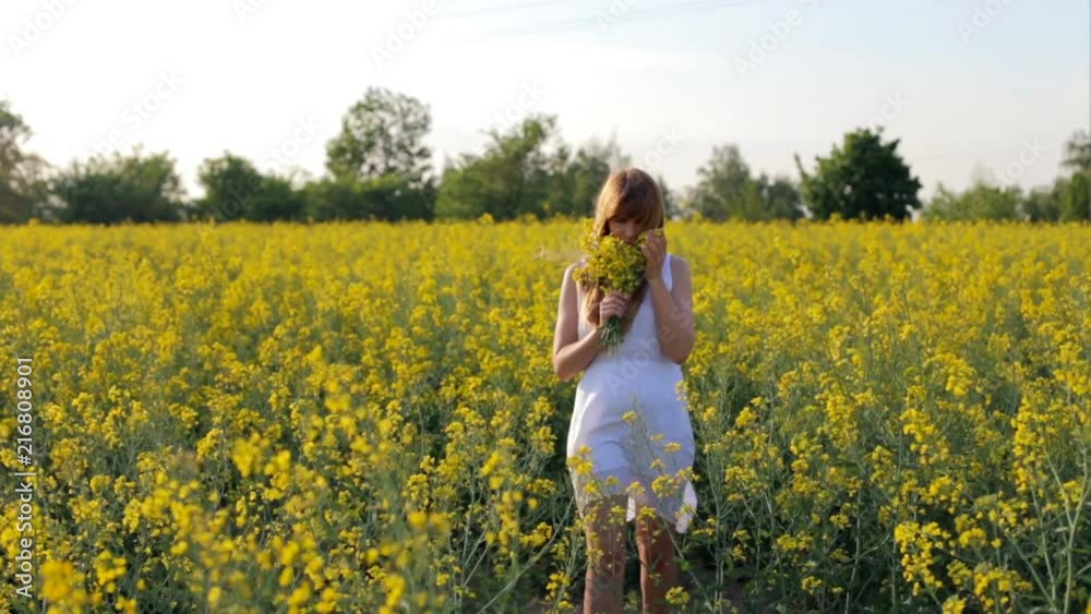 Beautiful girl in a white dress strolls along the flower field Beautiful girl in a white dress strolls along the flower field