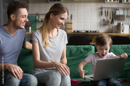 Amazed excited son happy to receive new laptop as birthday gift from smiling parents congratulating kid at home, child boy surprised to get unbelievable present from mom and dad - his first computer