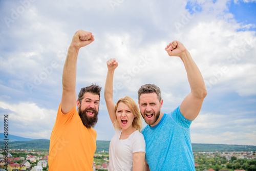Ways to build сohesive team. Woman and men look confident successful sky background. Threesome stand happy confidently with raised fists. Behaviors of cohesive team. Celebrate success. Yes we can