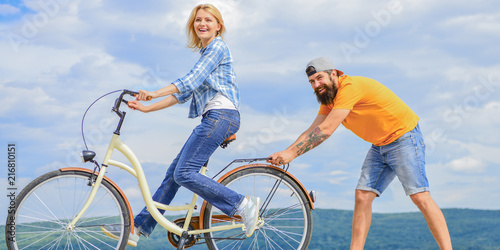 Teach adult to ride bike. Find balance. Woman rides bicycle sky background. How to learn to ride bike as an adult. Girl cycling while boyfriend support her. Man helps keep balance and ride bike