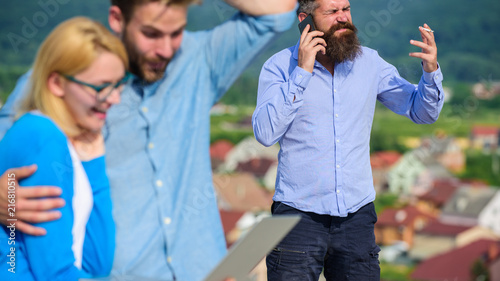 Couple colleagues flirting while boss busy with mobile conversation. Couple having fun while internet surfing outdoor. Mobile internet benefits. Colleagues use video conferencing instead mobile call