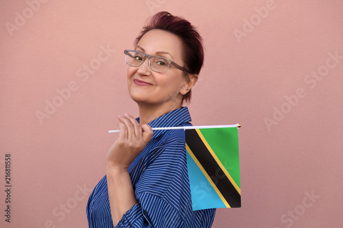 Tanzania flag. Woman holding Tanzanian flag. Nice portrait of middle aged lady 40 50 years old with a national flag over pink wall background outdoors.
