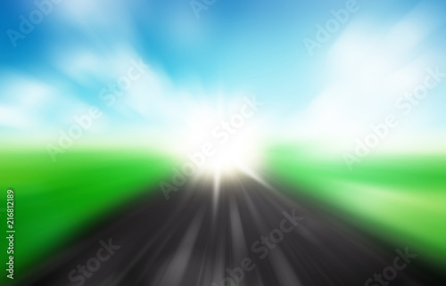 Blurred asphalt road and blue motion blurred sky with clouds and light spot