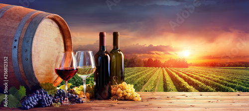 Fotografia, Obraz Bottles And Wineglasses With Grapes And Barrel In Rural Scene