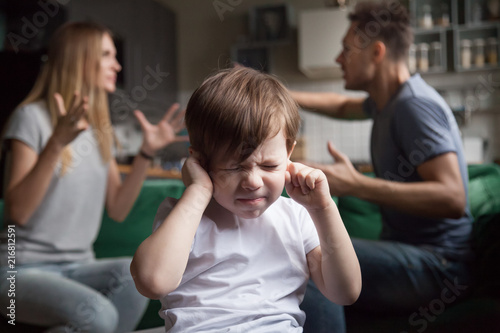 Frustrated kid son puts fingers in ears not listening to noisy parents arguing, stressed preschool boy suffering from mom and dad fighting shouting, family conflicts negative impact on child concept