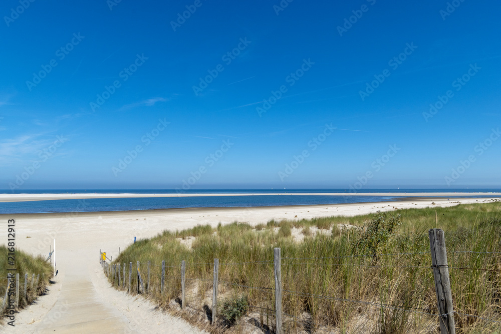 Path to the white beach with blue sea with white sailboats in the background. North Sea between Kijkduin and Ter Heijde, the Netherlands, Europe. Path to the white beach with blue sea with white sailboats in the background. North Sea between Kijkduin and Ter Heijde, the Netherlands, Europe.