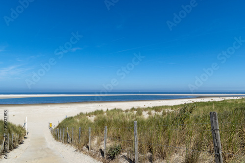 Path to the white beach with blue sea with white sailboats in the background. North Sea between Kijkduin and Ter Heijde, the Netherlands, Europe.