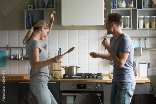 Fotografie Funny young couple dancing to music together enjoying cooking in the kitchen, ma