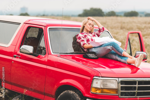beautiful young woman relaxing on hood of car in field