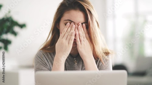 Young woman using computer and rubbing her eyes in front of desk photo