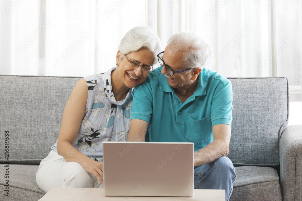 Smiling senior couple using laptop sitting on sofa