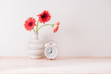 flowers and alarm clock on a white wall shelf