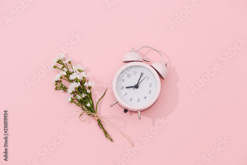 Wildflowers bouquet and retro alarm clock with shadow on pink background