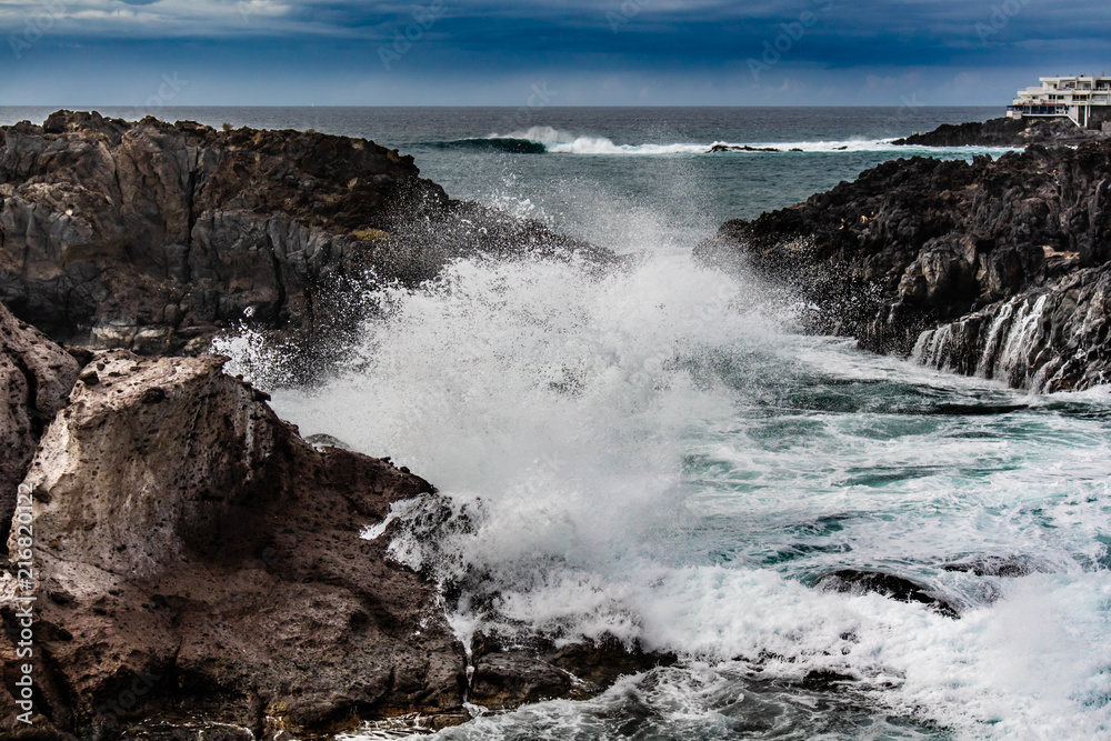 Fototapeta premium Seascape with black volcanic rocks, waves and splashes