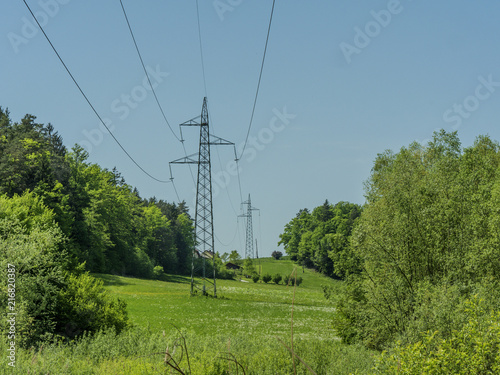 High voltage power electricity lines with high pilars going through green land.