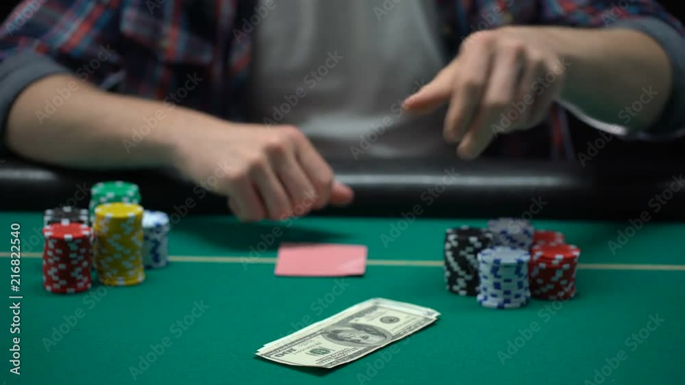 Poker player checking his cards and raising, putting dollars on table, all-in Poker player checking his cards and raising, putting dollars on table, all-in