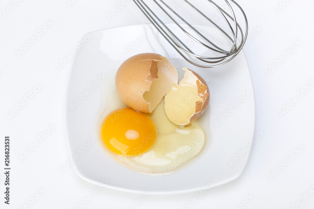 broken raw egg and wire mixing in a porcelain dish on a white broken raw egg and wire mixing in a porcelain dish on a white