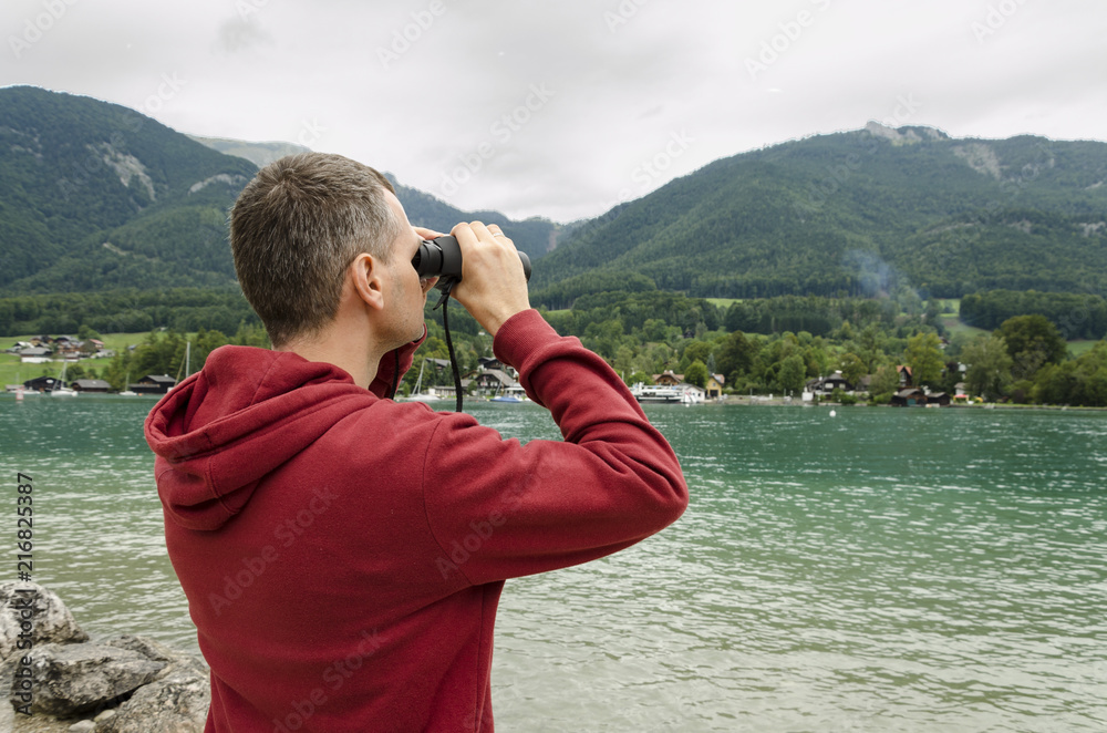 A middle-aged man with a binoculars observes the nature at the lake A middle-aged man with a binoculars observes the nature at the lake