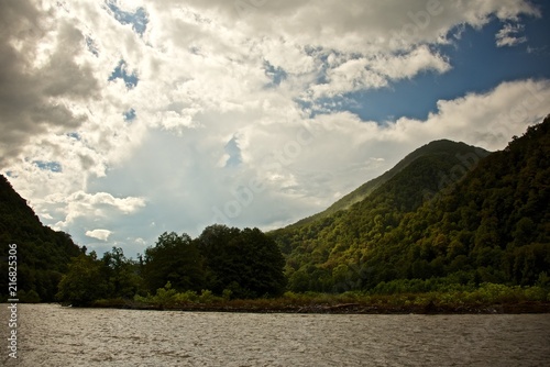 Summer landscape. Sky with clouds over mountain river. Mist over green forest.