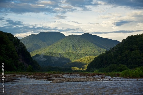 Summer landscape. Sky with clouds over mountain river. Mist over green forest.