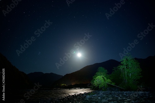 The moon over mountains at night. Wide valley of the river. © German