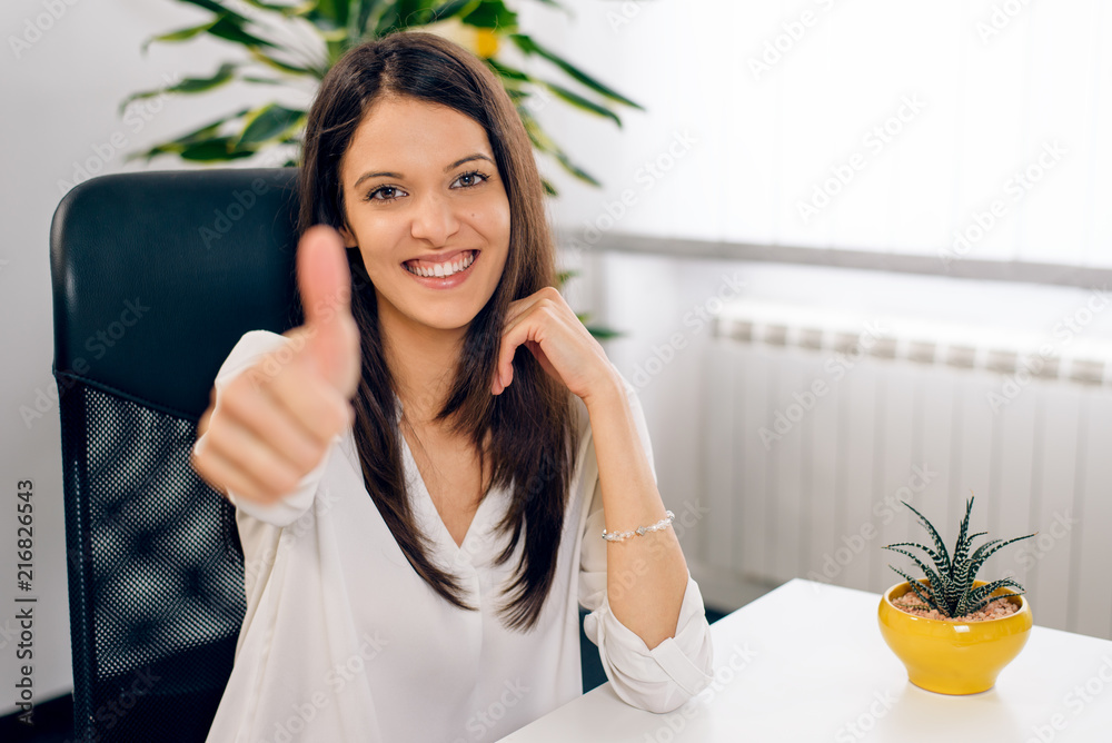 Portrait of young business woman at modern startup office interior showing thumbs up