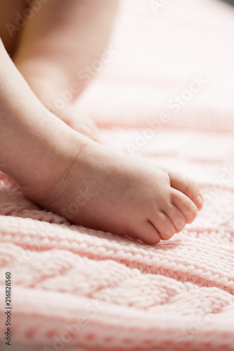 Close up of newborn baby feet. Baby legs on a pink background. The legs of a child on a knitted plaid. Cozy.