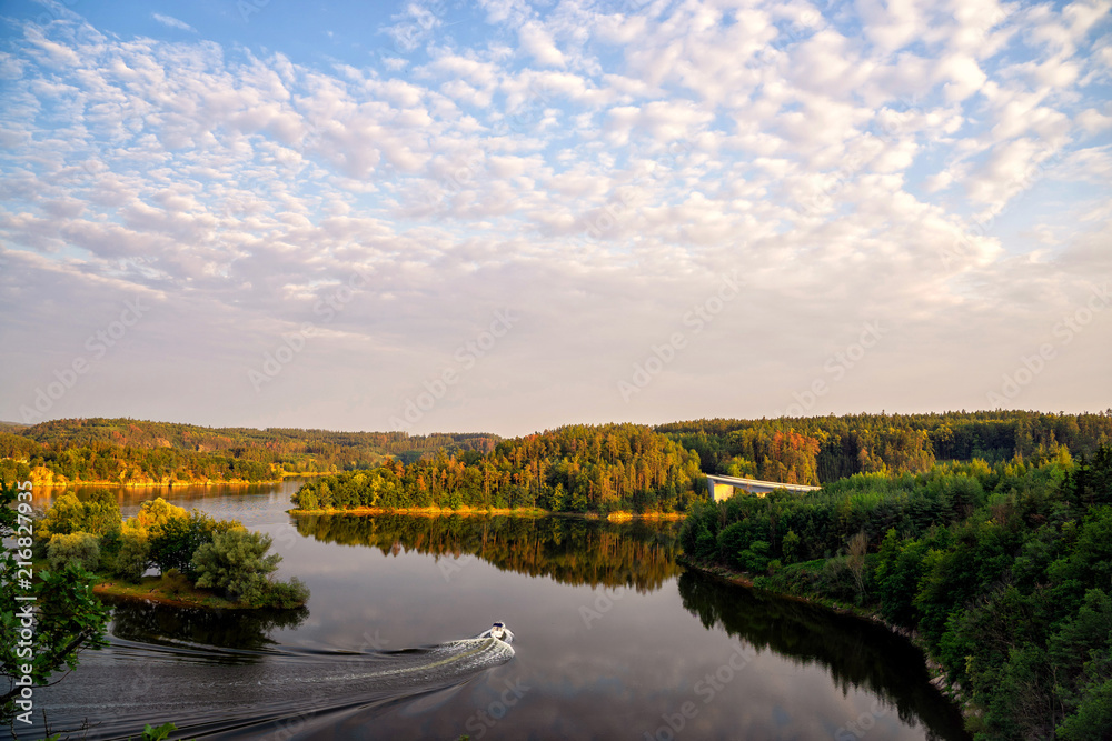 Fototapeta premium Colourful sunset over a lake. Summer scene of wide river landscape with setting sun. Small boat sails in river.