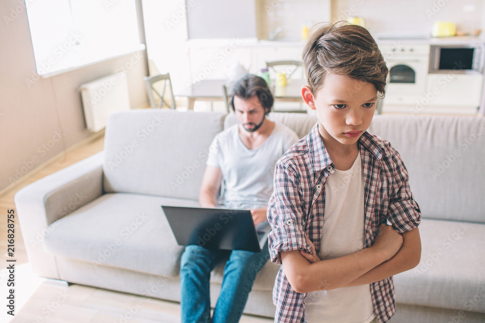 Man sits on sofa and holds laptop. He works. Boy is unhappy and sad. He holds his hands crossed. Boy feels lonely.