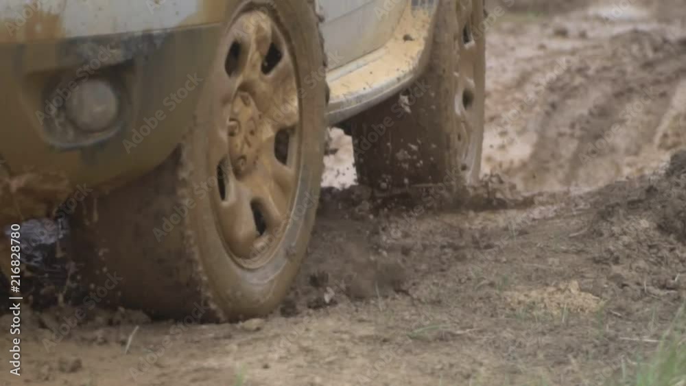 Powerful towed off-road vehicle on dirty rural road after rain close-up in bad weather. Big dirty tires and headlights, clods of clay flying off on the grass. Powerful towed off-road vehicle on dirty rural road after rain close-up in bad weather. Big dirty tires and headlights, clods of clay flying off on the grass.