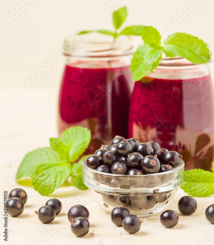 Currant smoothie decorated with fresh green mint leaves and raw ripe berries on yellow pastel background.