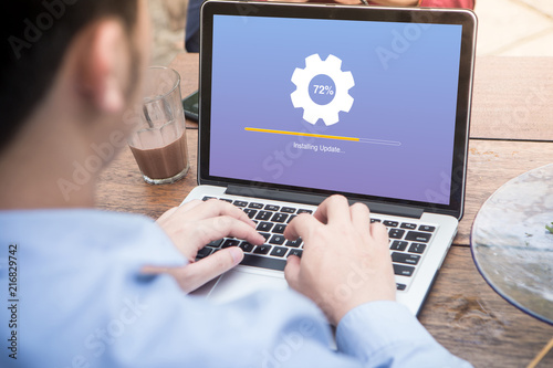 Young man waiting for installing update process with gearbox percentage progress and loading bar on laptop / computer at the outdoor cafe