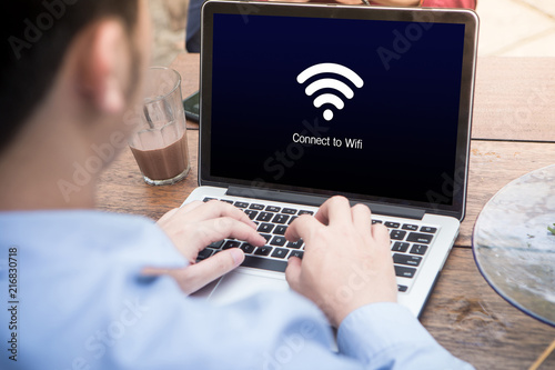 Young man working and waiting for wi-fi connection using laptop / computer at the outdoor cafe