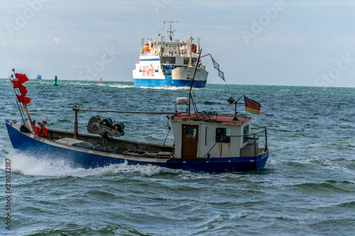 Small fishing boat on the ocean with a ferry in the background heading to the horizon
