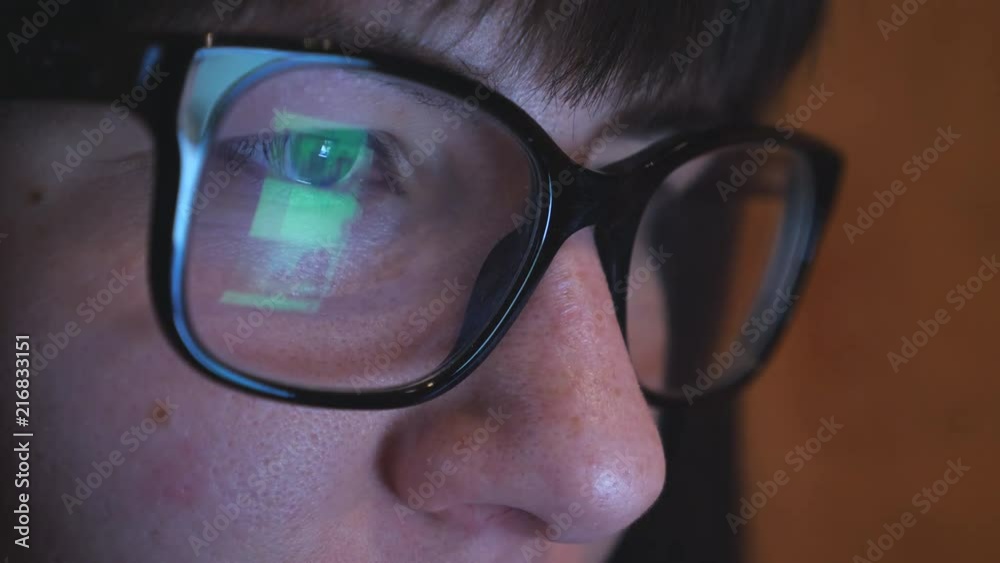 Young woman in glasses looking at the smartphone and surfing the internet. Screen of phone is reflected in the eyeglasses. Close up of female face Young woman in glasses looking at the smartphone and surfing the internet. Screen of phone is reflected in the eyeglasses. Close up of female face