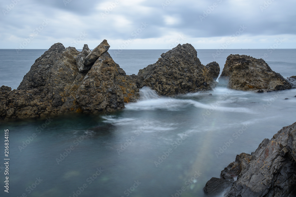 A group of rocks at the atlantic ocean surrounded by calm waters in a cloudy day at the Basque Country, Spain A group of rocks at the atlantic ocean surrounded by calm waters in a cloudy day at the Basque Country, Spain