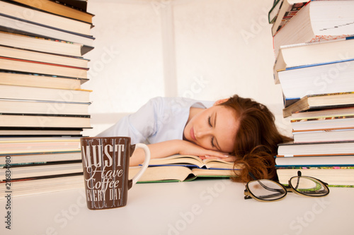 Bild auf Leinwand attractive beautiful tired student sleeps on pile of books with a coffee mug on