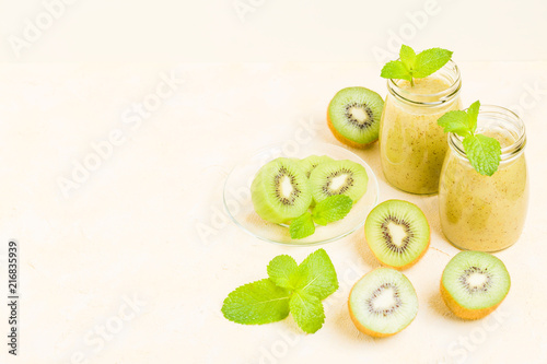 Kiwi smoothie decorated with fresh green mint leaves and raw ripe cut fruit on yellow pastel background.