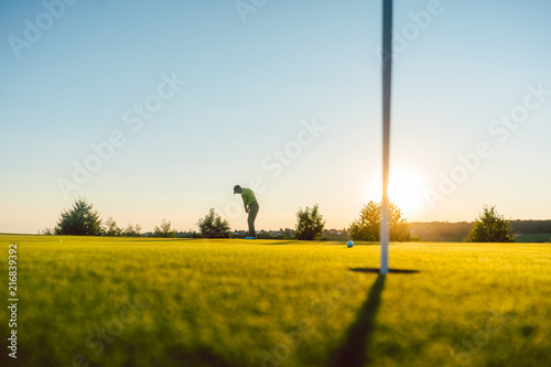 Full length view of the silhouette of a male player, hitting a long shot on the putting green of a professional golf course of a modern country club photo