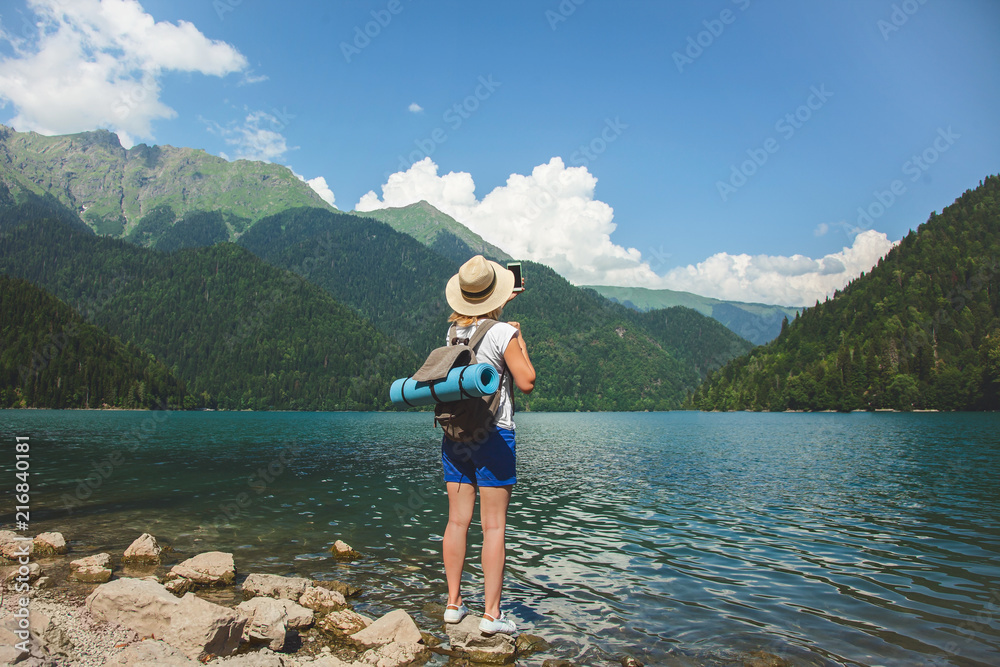 Beautiful girl traveler in a hat stands on a lake in the background of the mountains