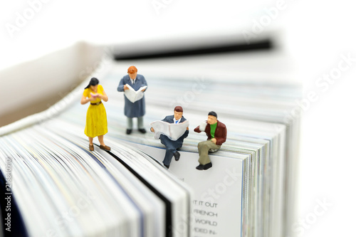 Miniature people: Businessman reading newspaper and sitting on book using as background education or business concept.