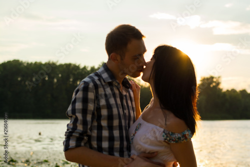 The man is kisses the young woman and hugs her at sunset background, blurred. © allai