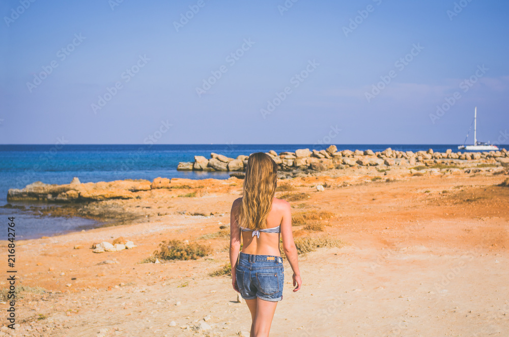 Young woman walking in summer on the beach against the sea