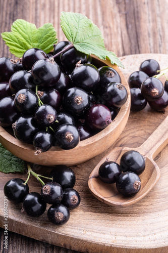 Fresh ripe black currant in wooden bowl with original leaves and spoon on rustic old background close-up