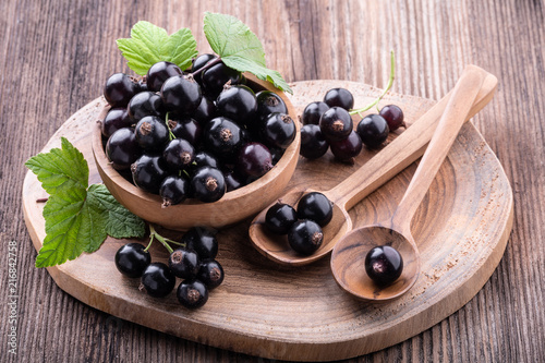 Fresh ripe black currant in wooden bowl with original leaves and tow spoons on rustic old background close-up