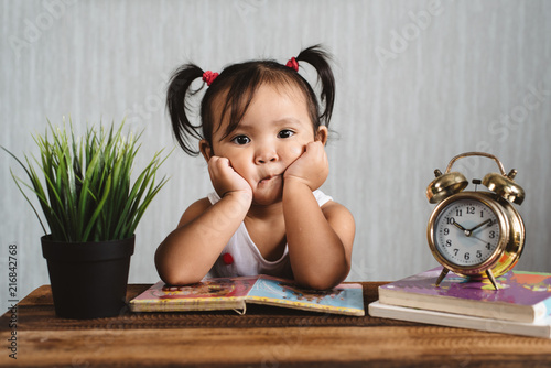 cute little asian baby toddler making boring face while reading books with alarm clock. child growth, early education and learning concept photo