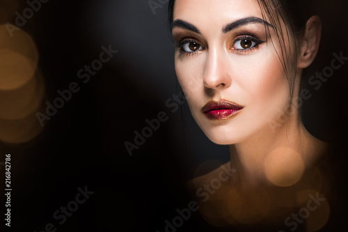 portrait of attractive woman with makeup posing on black with golden bokeh