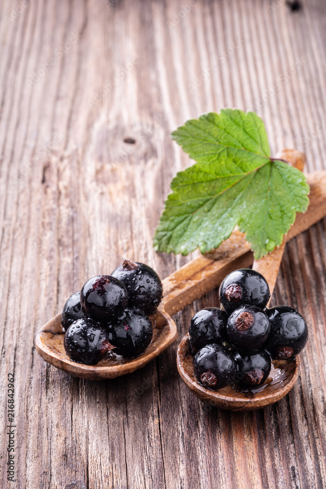 Two wooden spoons with fresh black currant and green leaf on rustic old background. Two wooden spoons with fresh black currant and green leaf on rustic old background.