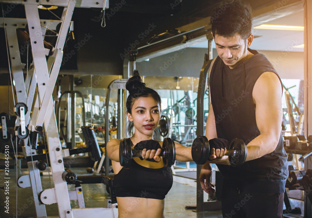 Asian people Sport girl doing weight exercises working with heavy dumbbells her personal trainer at Gym workout Asian people Sport girl doing weight exercises working with heavy dumbbells her personal trainer at Gym workout